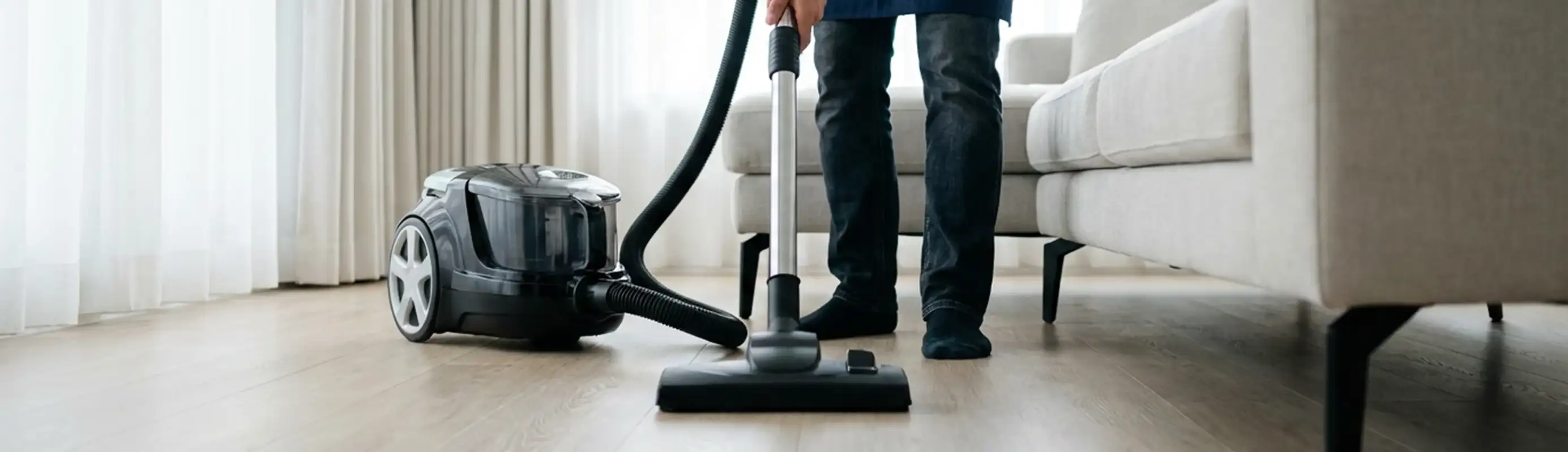 Professional house cleaner vacuuming a living room floor with a canister vacuum cleaner, Miami, FL.