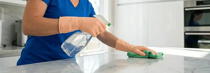 Maid service worker spraying and wiping a kitchen countertop with a microfiber cloth for sanitizing, Miami, FL.