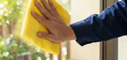 House cleaner wiping a glass window with a yellow microfiber cloth for streak-free cleaning, Miami, FL.